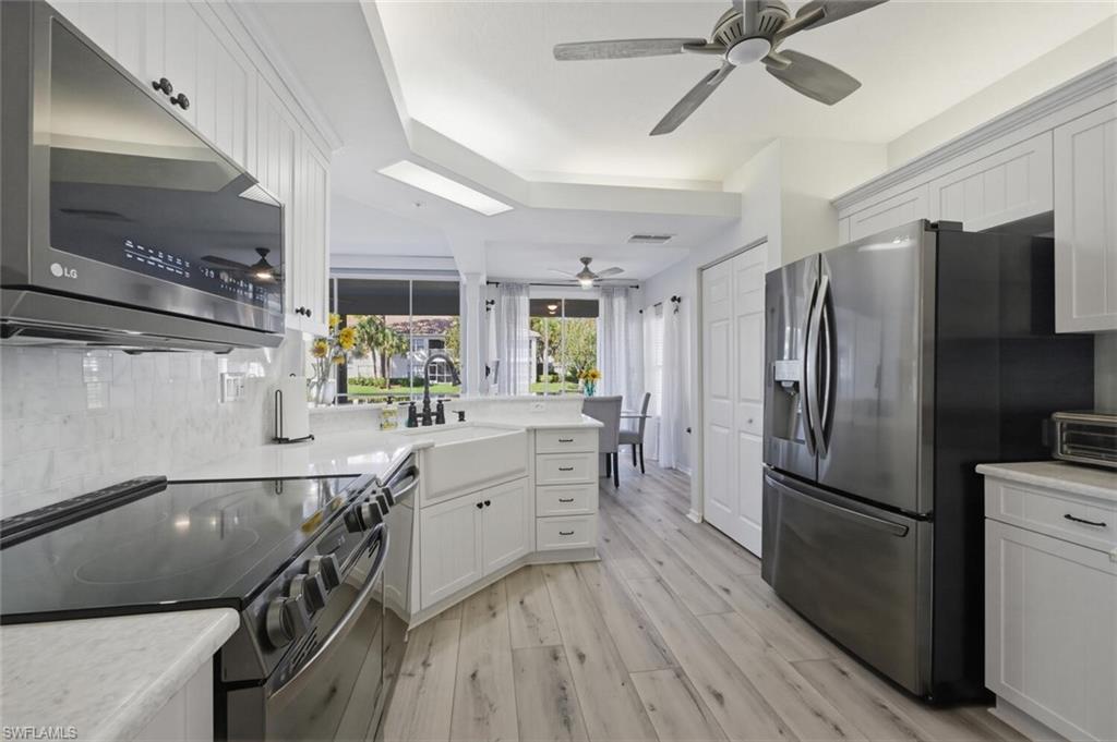 6899 Rain Lily Road, Unit 103 Naples, FL 34109 - Photo 12 of 39 Kitchen with stainless steel appliances, white cabinetry, light wood finished floors, a peninsula, and light stone counters