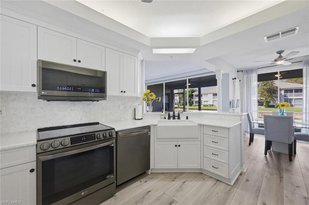 6899 Rain Lily Road, Unit 103 Naples, FL 34109 - Photo 13 of 39 Kitchen featuring a peninsula, stainless steel appliances, ceiling fan, white cabinets, and light wood-type flooring