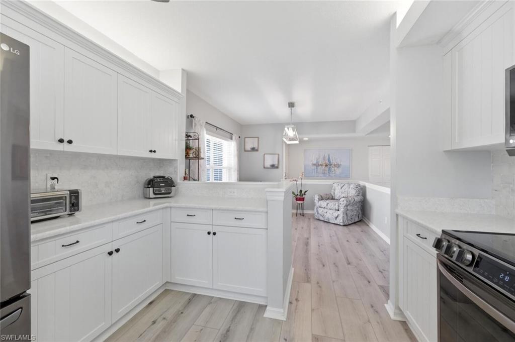 6899 Rain Lily Road, Unit 103 Naples, FL 34109 - Photo 15 of 39 Kitchen with decorative backsplash, light wood finished floors, a peninsula, white cabinetry, and stainless steel appliances