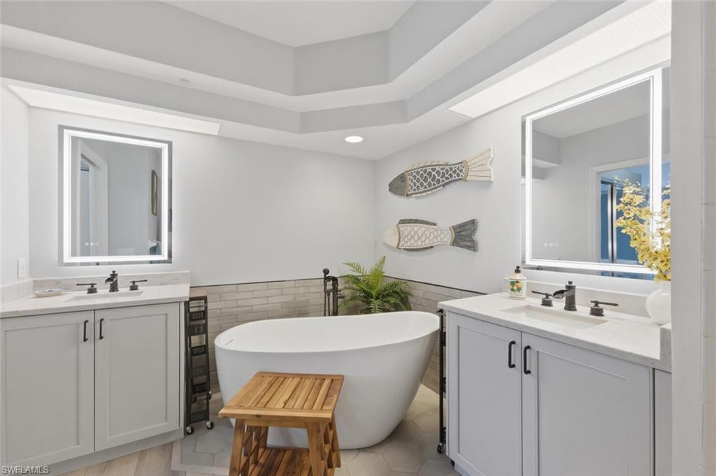 6899 Rain Lily Road, Unit 103 Naples, FL 34109 - Photo 20 of 39 Bathroom featuring two vanities, a wainscoted wall, tile walls, a freestanding bath, and light tile patterned flooring