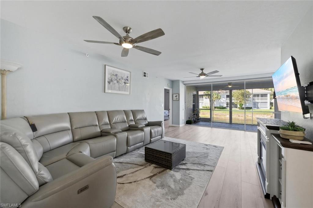 6899 Rain Lily Road, Unit 103 Naples, FL 34109 - Photo 6 of 39 Living room featuring light wood-type flooring, a ceiling fan, and expansive windows