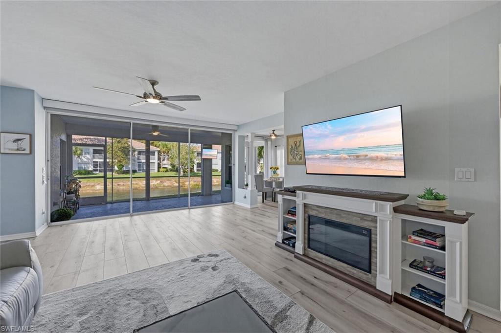6899 Rain Lily Road, Unit 103 Naples, FL 34109 - Photo 7 of 39 Living room featuring ceiling fan, light wood-type flooring, and a glass covered fireplace