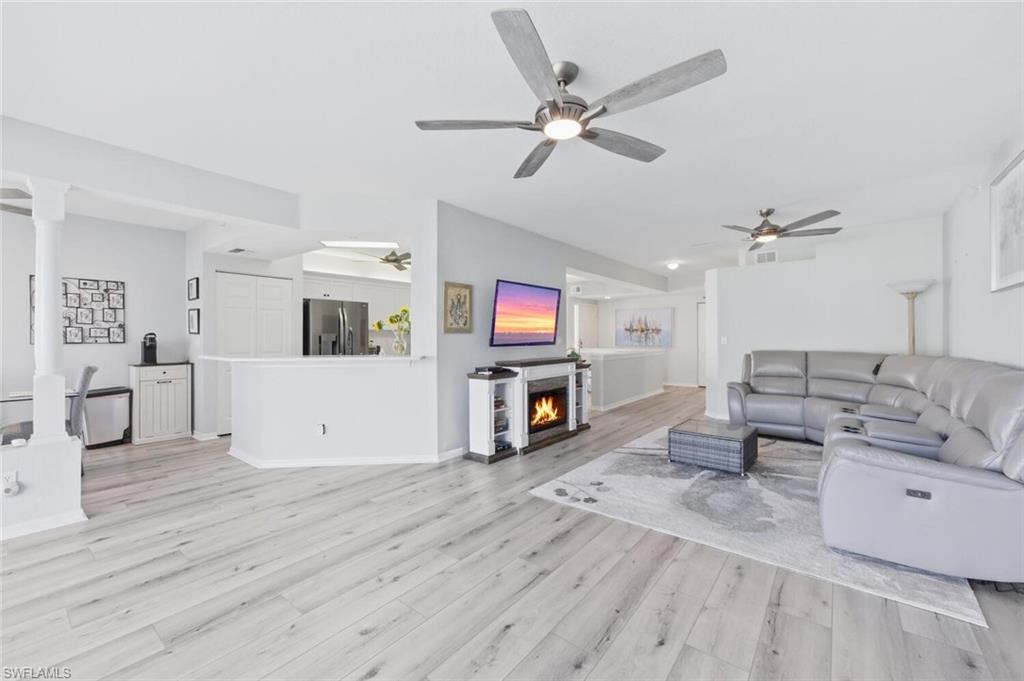 6899 Rain Lily Road, Unit 103 Naples, FL 34109 - Photo 9 of 39 Living area with a warm lit fireplace, light wood-style flooring, and ceiling fan