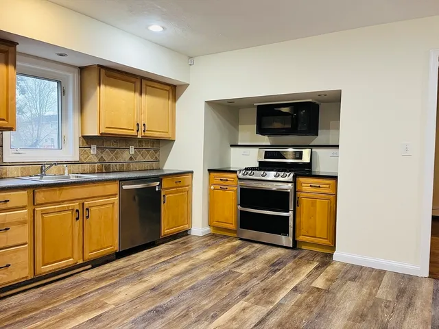 a kitchen with granite countertop wooden floors stainless steel appliances and a sink