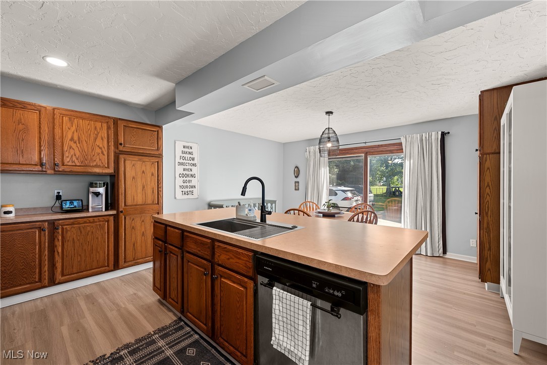 1605 Lander Road Cleveland, OH 44124 - Photo 5 of 38 Kitchen with stainless steel dishwasher, a textured ceiling, brown cabinetry, light countertops, and a center island with sink