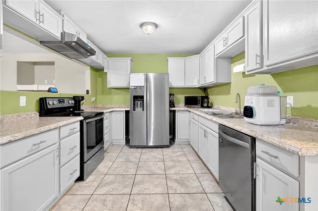 a kitchen with stainless steel appliances kitchen island granite countertop a refrigerator a sink dishwasher a stove with wooden cabinets