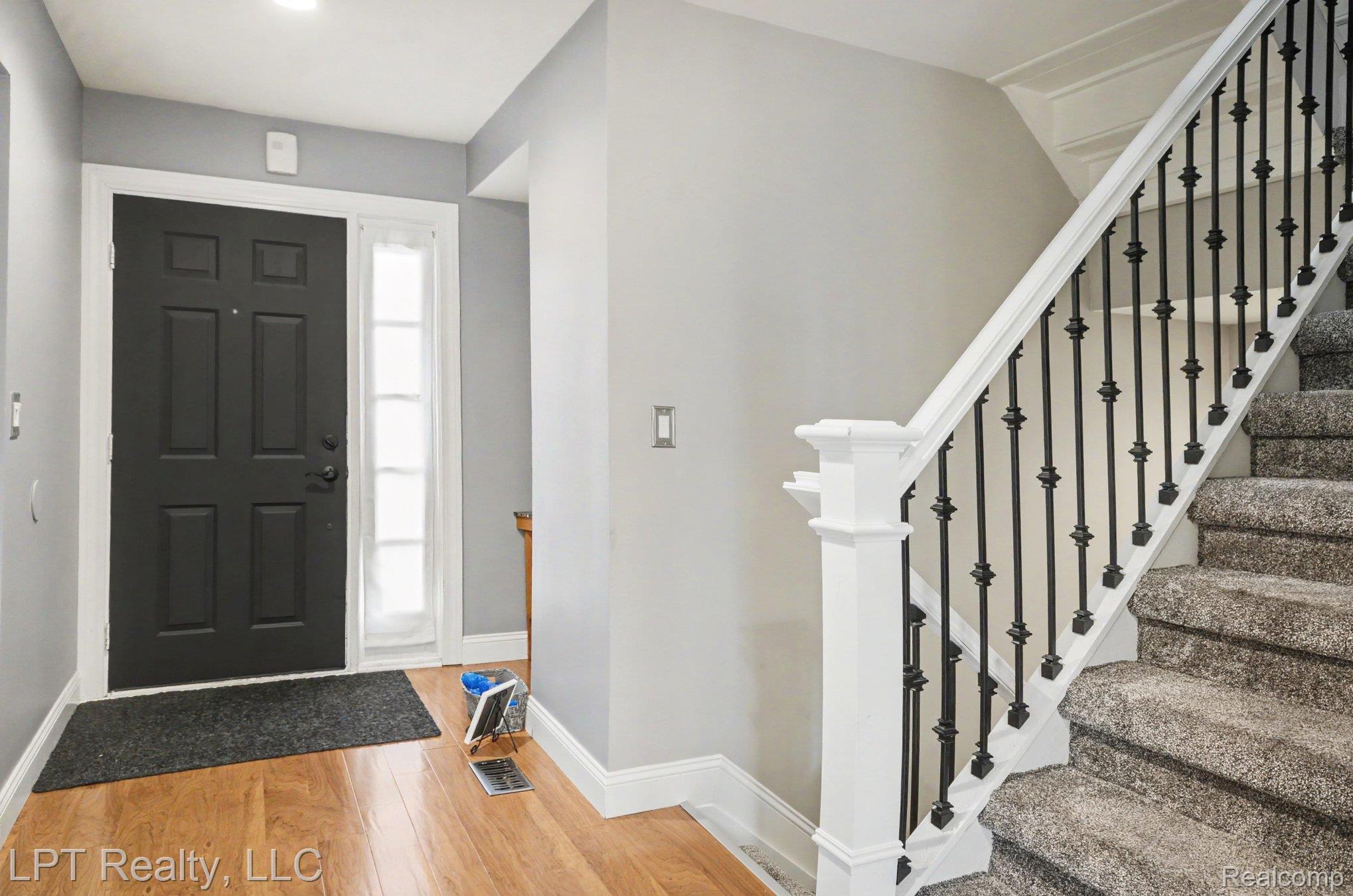 829 Langdon Court Rochester, MI 48307 - Photo 4 of 31 Entryway featuring LVP flooring, a six-panel black door with a sidelight, and a staircase with wrought iron balusters and carpeted treads