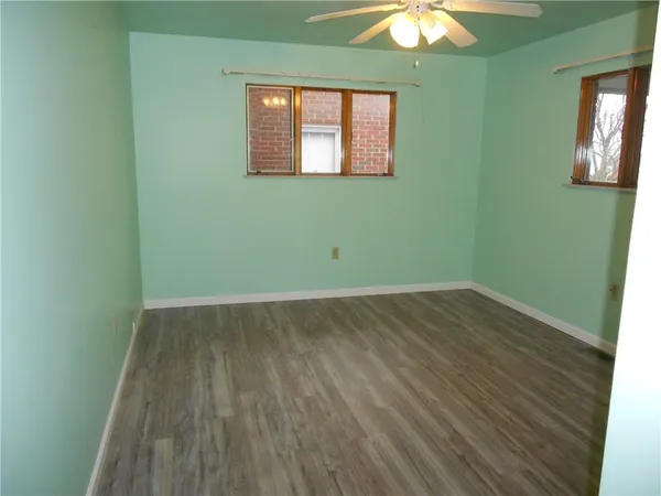 an empty room with a chandelier fan and wooden floor