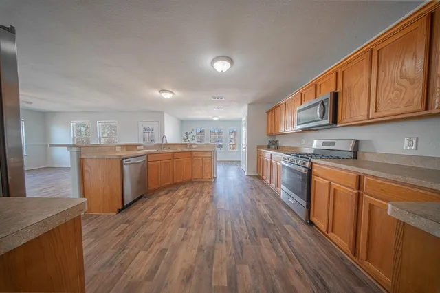 a kitchen with stainless steel appliances granite countertop wooden floors and view of living room