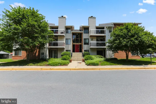a front view of a multi story residential apartment building with a yard and large trees