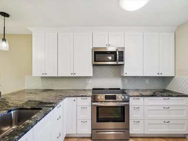 a kitchen with granite countertop a stove a sink and a white cabinets