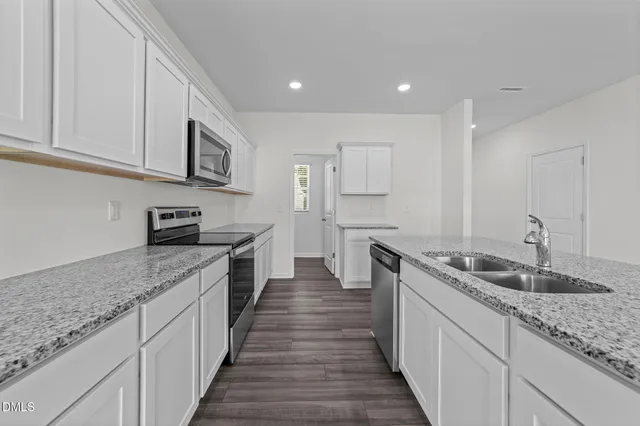 a large white kitchen with kitchen island a sink wooden floor and a refrigerator