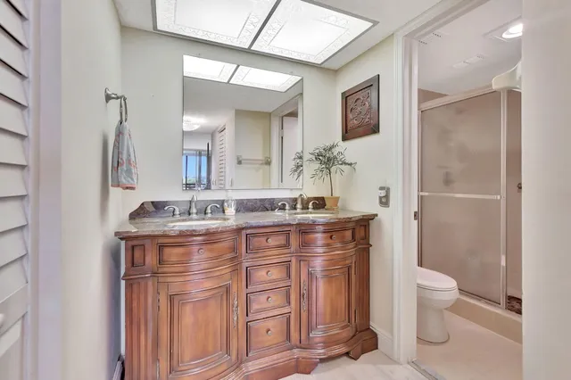 a bathroom with a granite countertop sink a toilet a mirror and shower