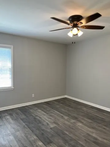 an empty room with wooden floor fan and windows