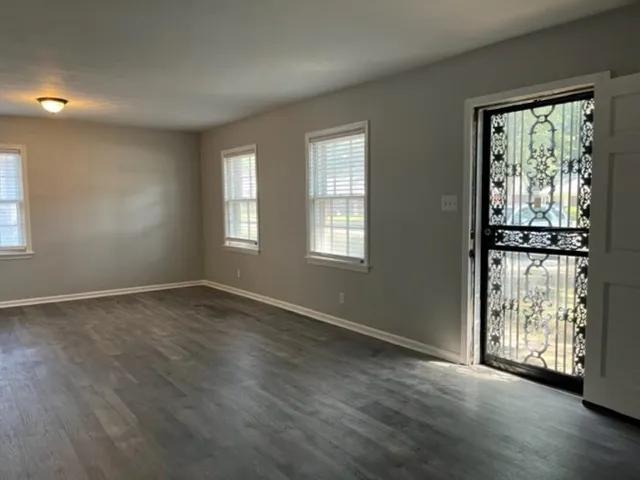 a view of an empty room with wooden floor and a window