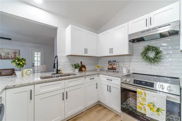a kitchen with a sink dishwasher a stove and white cabinets with wooden floor