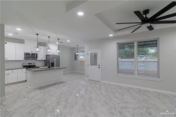 a large white kitchen with stainless steel appliances granite countertop a stove a sink a refrigerator with white cabinets and wooden floor