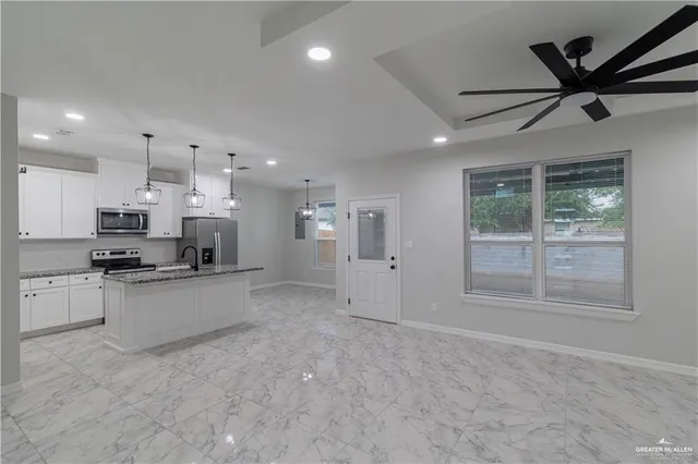 a large white kitchen with stainless steel appliances granite countertop a stove a sink a refrigerator with white cabinets and wooden floor