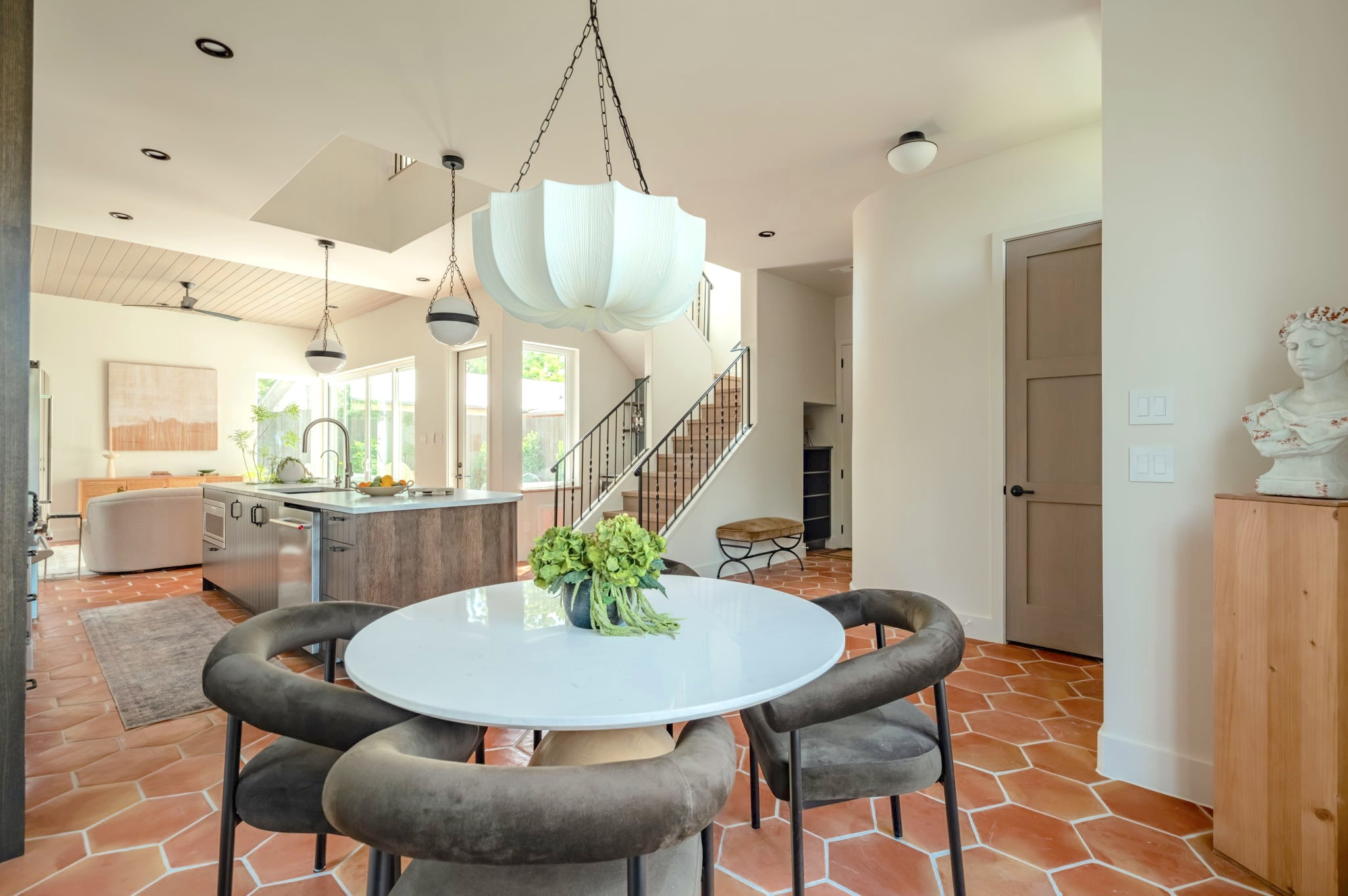 4713 Bolm Road Austin, TX 78702 - Photo 5 of 40 Open-concept kitchen and dining area featuring hexagonal terracotta-style floor tiling, a central kitchen island with a stone countertop, a contemporary white dining table, a prominent white chandelier, and a staircase with metal railings