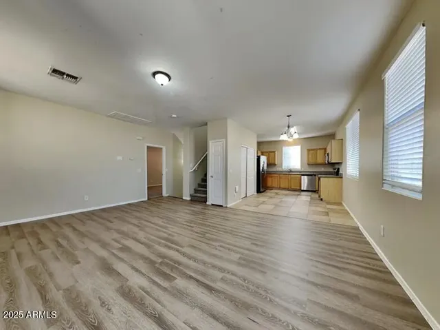 an empty room with wooden floor kitchen view and windows