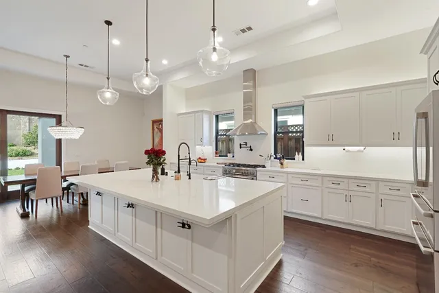 a large white kitchen with cabinets a sink a center island and stainless steel appliances