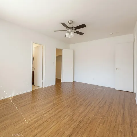 an empty room with wooden floor a ceiling fan and windows