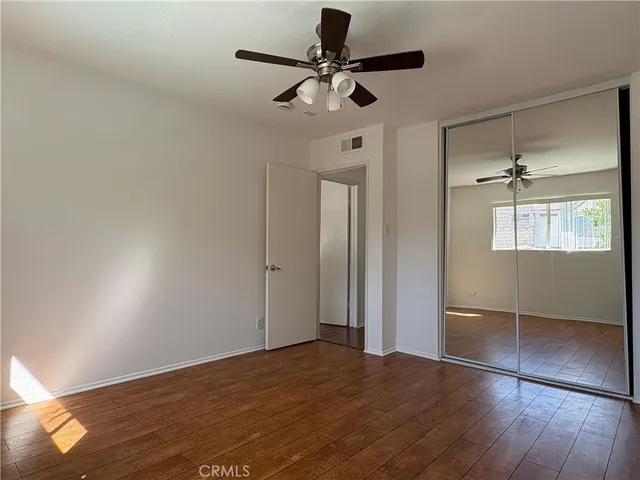 a view of an empty room with wooden floor and a ceiling fan