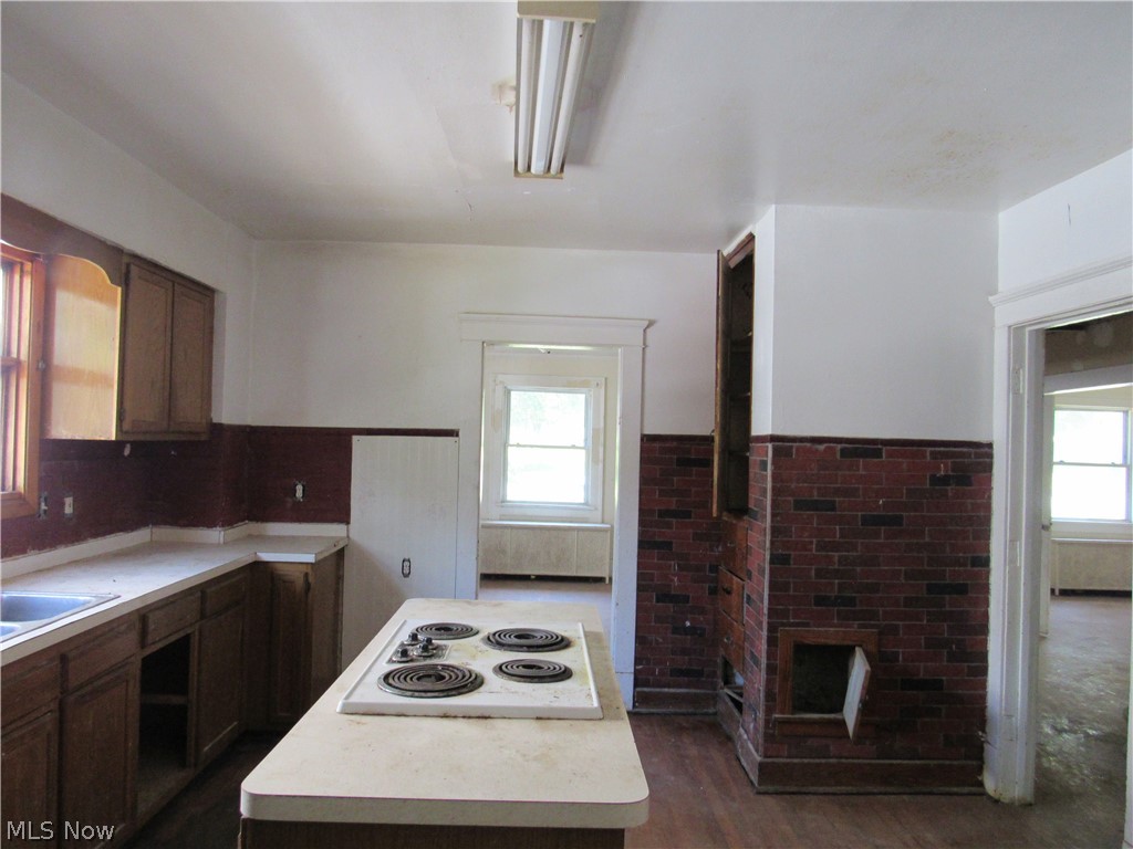 1726 Lee Road Cleveland Heights, OH 44118 - Photo 8 of 36 Kitchen featuring a central island with an integrated cooktop, wood-finish flooring, and a brick-accented wall with built-in shelving