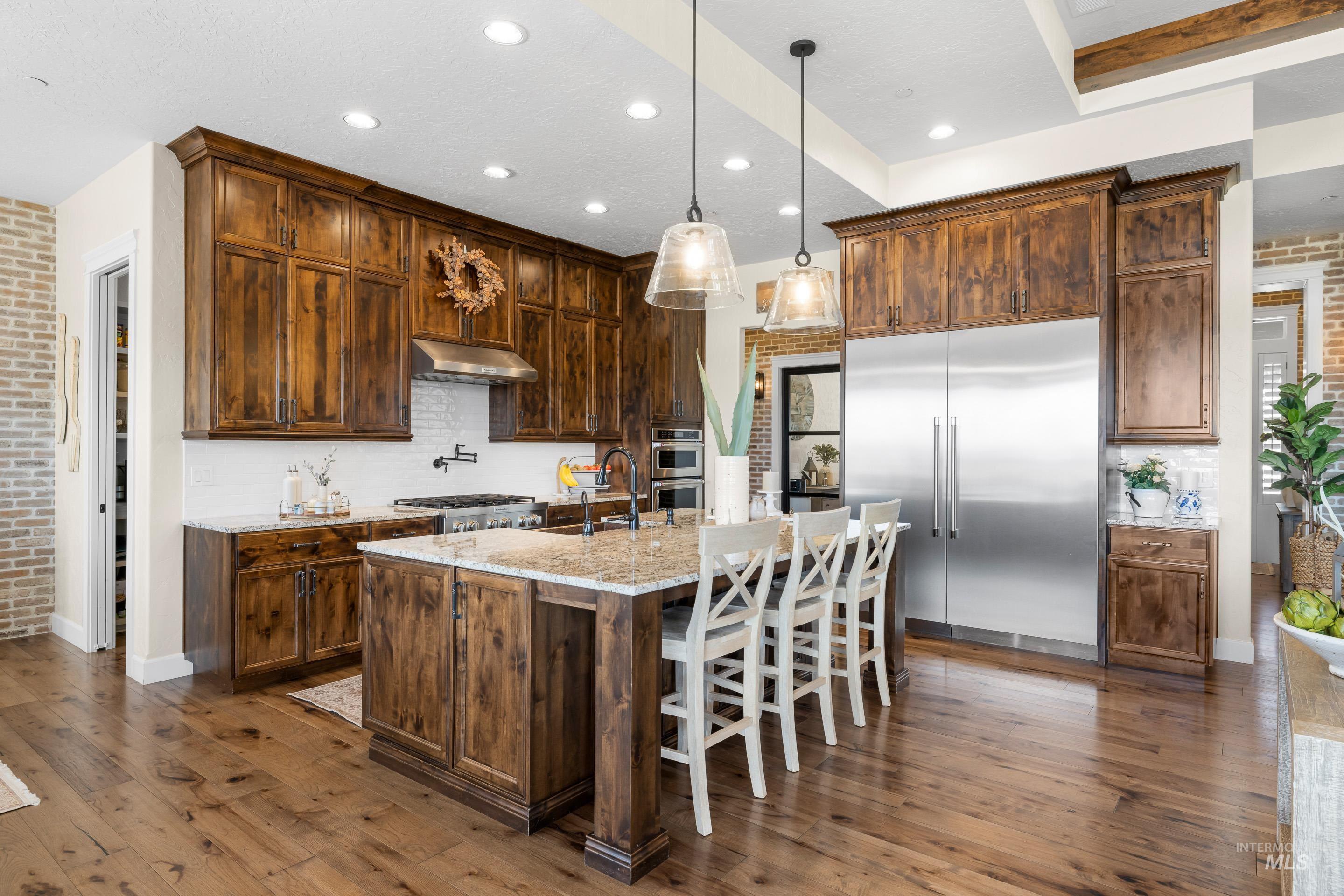 9819 Foothill Road Middleton, ID 83644 - Photo 19 of 50 Kitchen with brick wall, appliances with stainless steel finishes, decorative backsplash, dark wood finished floors, and light stone counters