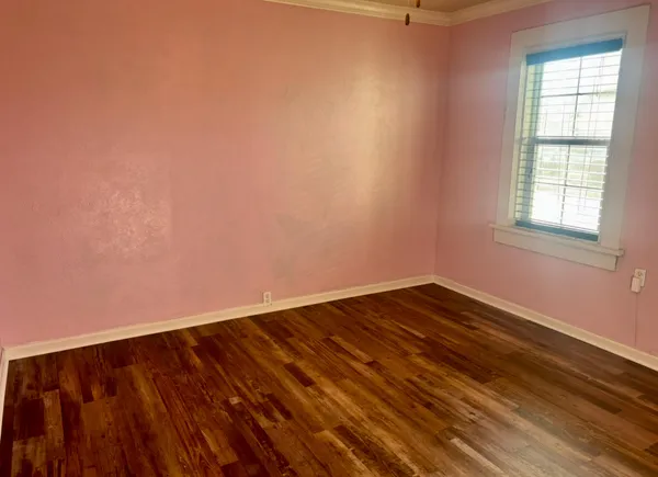 a view of an empty room with wooden floor and a window