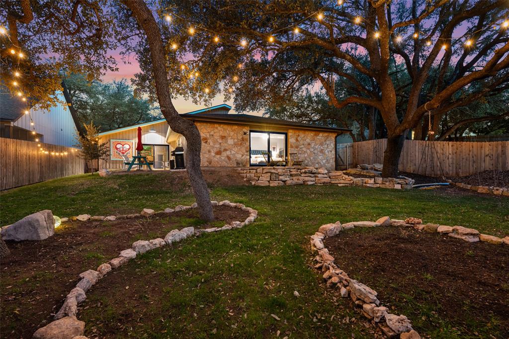2210 Red Fox Road Austin, TX 78734 - Photo 1 of 40 Mature trees and string lighting illuminate this inviting backyard retreat with stone pathways.