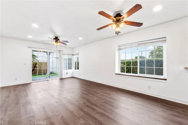 a view of an empty room with wooden floor and a ceiling fan