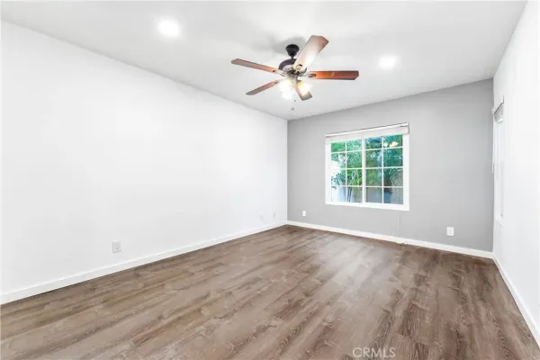 an empty room with wooden floor fan and windows