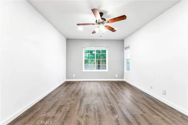 an empty room with wooden floor fan and windows