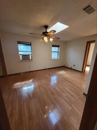 an empty room with wooden floor chandelier fan and windows
