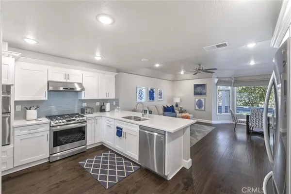 a kitchen with stainless steel appliances a sink a stove a refrigerator cabinets and a dining table with wooden floor