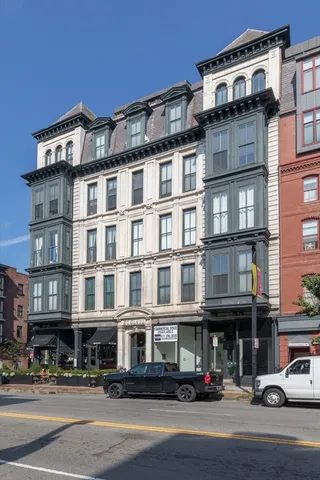 a front view of a building with lot of cars and trees