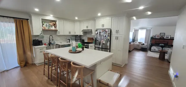 a kitchen with stainless steel appliances granite countertop a refrigerator a microwave a stove a sink a dining table and chairs with wooden floor
