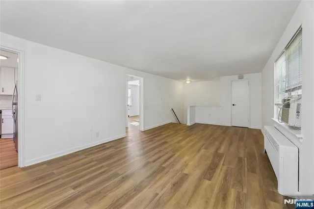 a view of empty room with wooden floor and kitchen