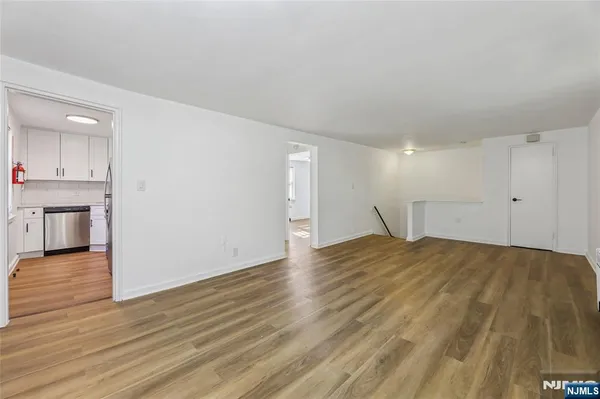 a view of empty room with wooden floor and kitchen