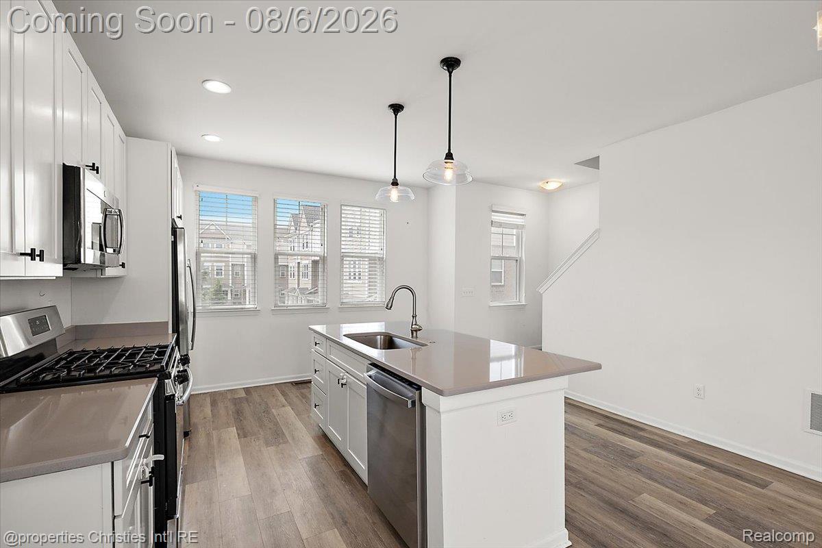Modern kitchen featuring white shaker cabinetry, stainless steel appliances, a center island with sink, and wood-finish flooring