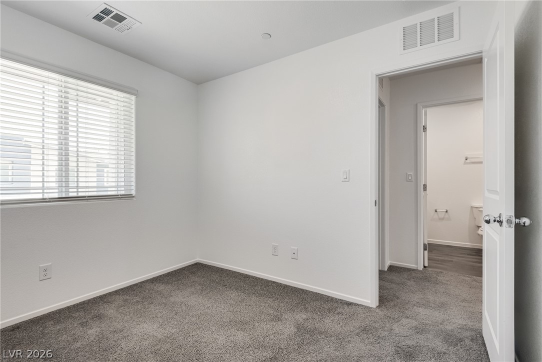 1114 Scarlet Sparrow Street Henderson, NV 89011 - Photo 23 of 25 A well-lit bedroom features plush carpeting and a convenient en-suite bathroom access.
