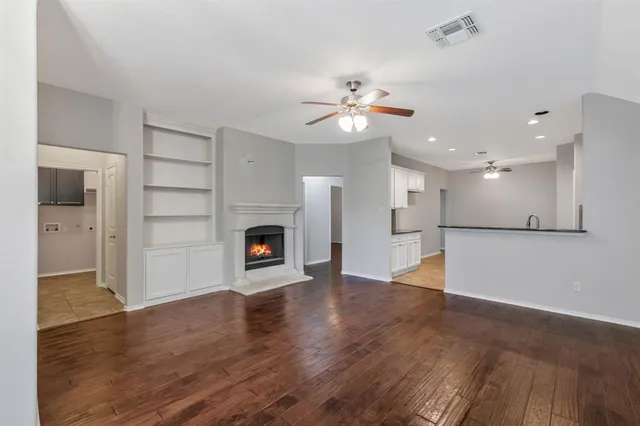 an empty room with wooden floor fireplace and kitchen view