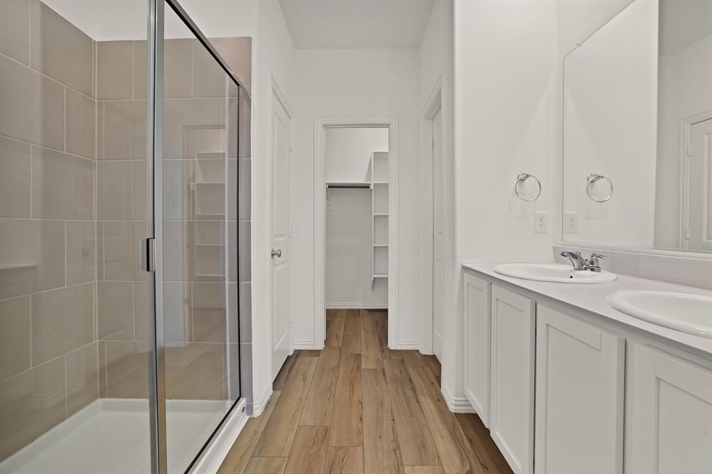 3204 Renaissance Drive Denton, TX 76207 - Photo 14 of 25 Bathroom featuring a glass-enclosed shower with neutral tile surround, dual vanity with undermount sinks, wood-finish flooring, and built-in closet shelving