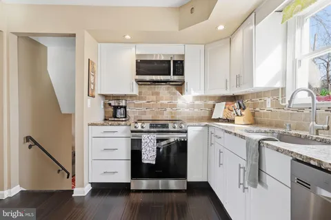 a kitchen with stainless steel appliances granite countertop a stove top oven a sink dishwasher and a refrigerator with wooden floor