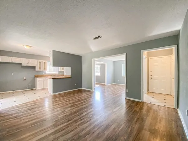 a view of an empty room and kitchen with wooden floor
