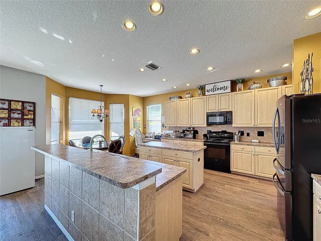 a kitchen with stainless steel appliances granite countertop a refrigerator a stove a sink and a dining table with wooden floor