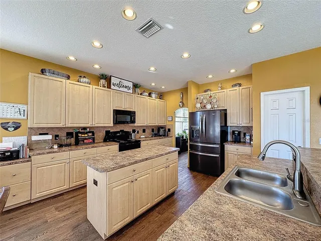 a view of a kitchen with kitchen island granite countertop a refrigerator a stove a sink a dining table and chairs with wooden floor