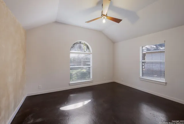 an empty room with wooden floor chandelier fan and windows