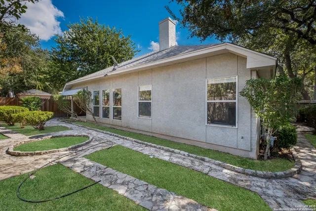 a white house with a small yard plants and large tree
